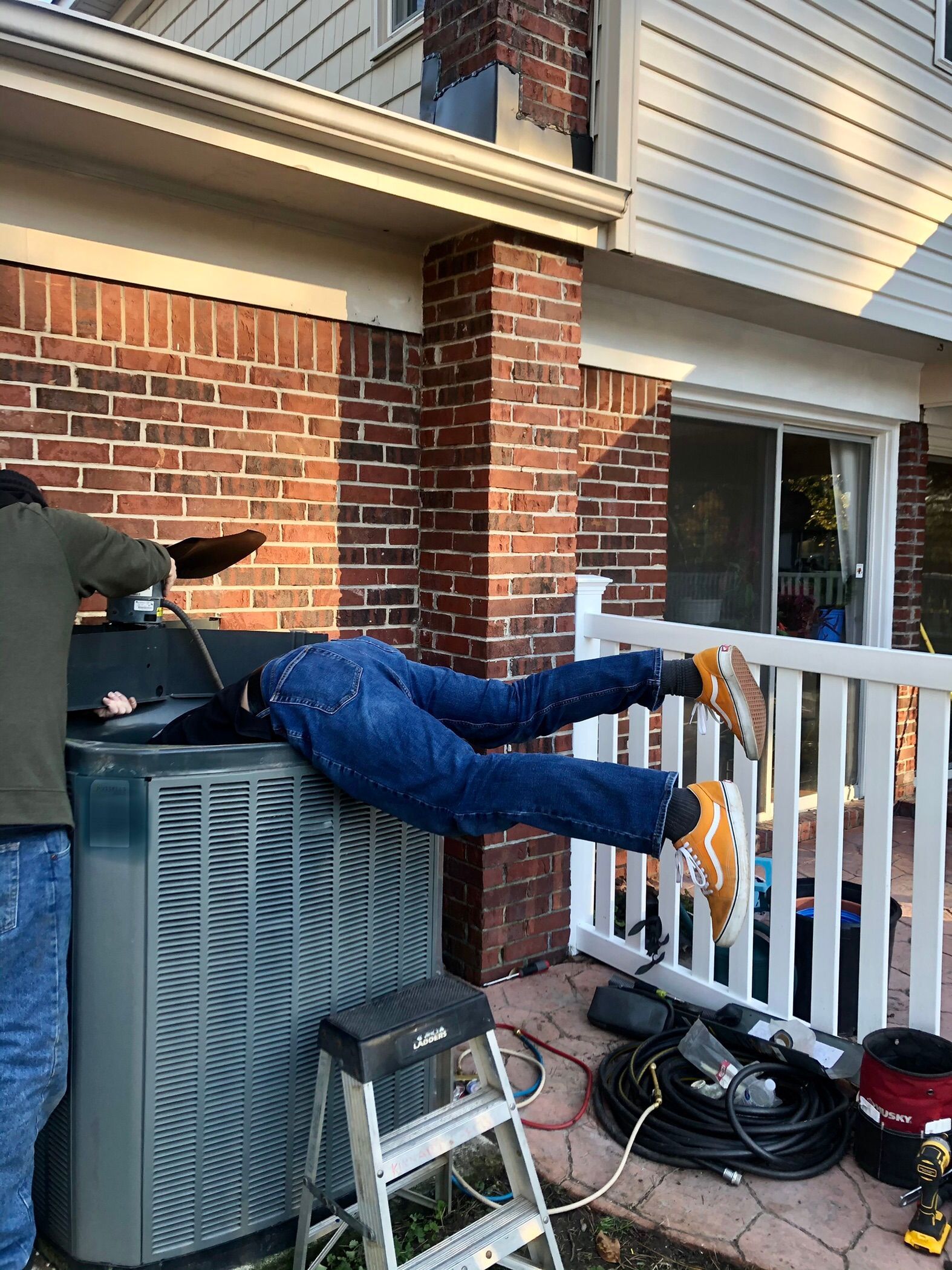 a man is laying on top of an air conditioner outside of a house