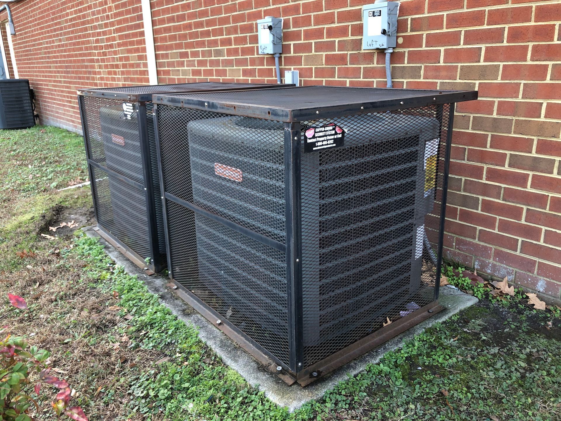 two air conditioners are sitting in a cage outside of a brick building