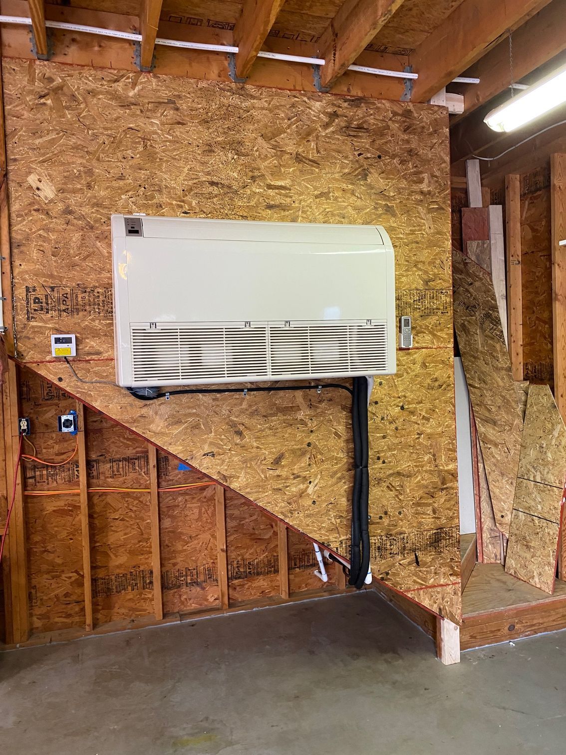 a white air conditioner is hanging on a wooden wall under a staircase