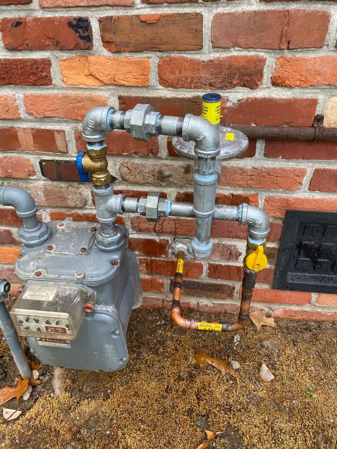 a gas meter is sitting on the ground next to a brick wall