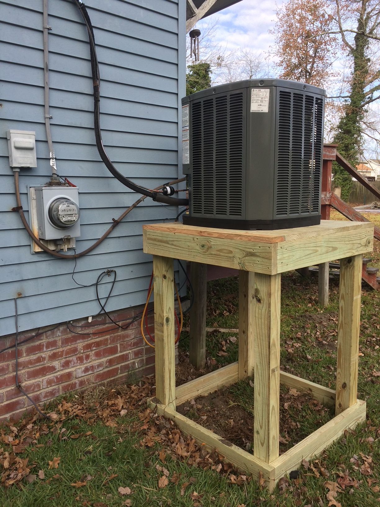 an air conditioner is sitting on top of a wooden stand next to a house