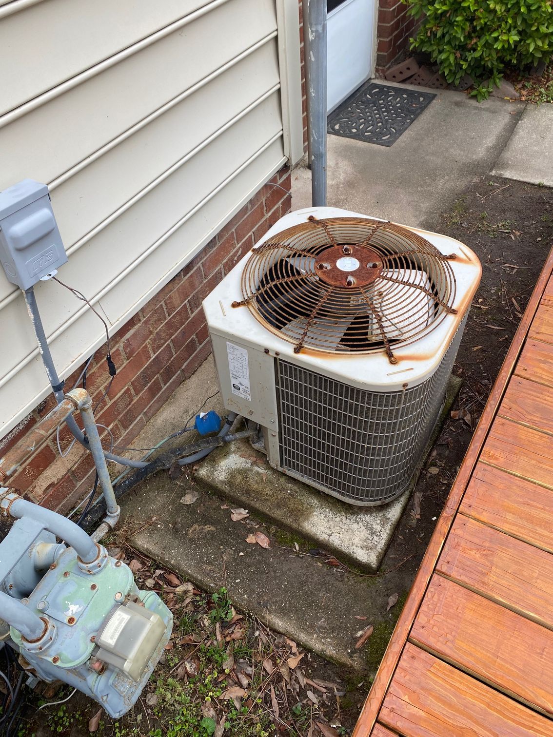 an old air conditioner is sitting on the side of a house next to a wooden deck