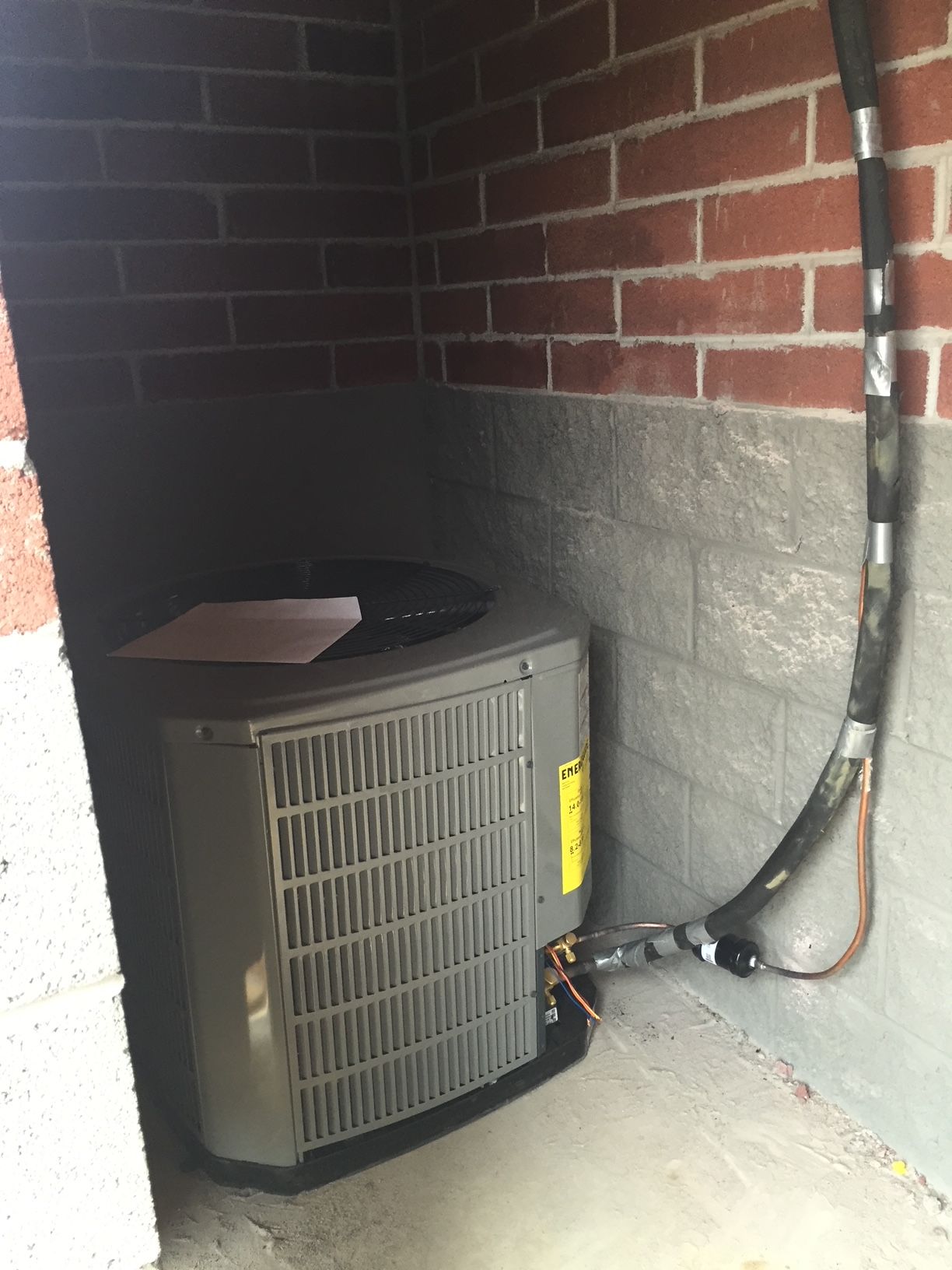 an air conditioner is sitting in a corner of a room next to a brick wall 