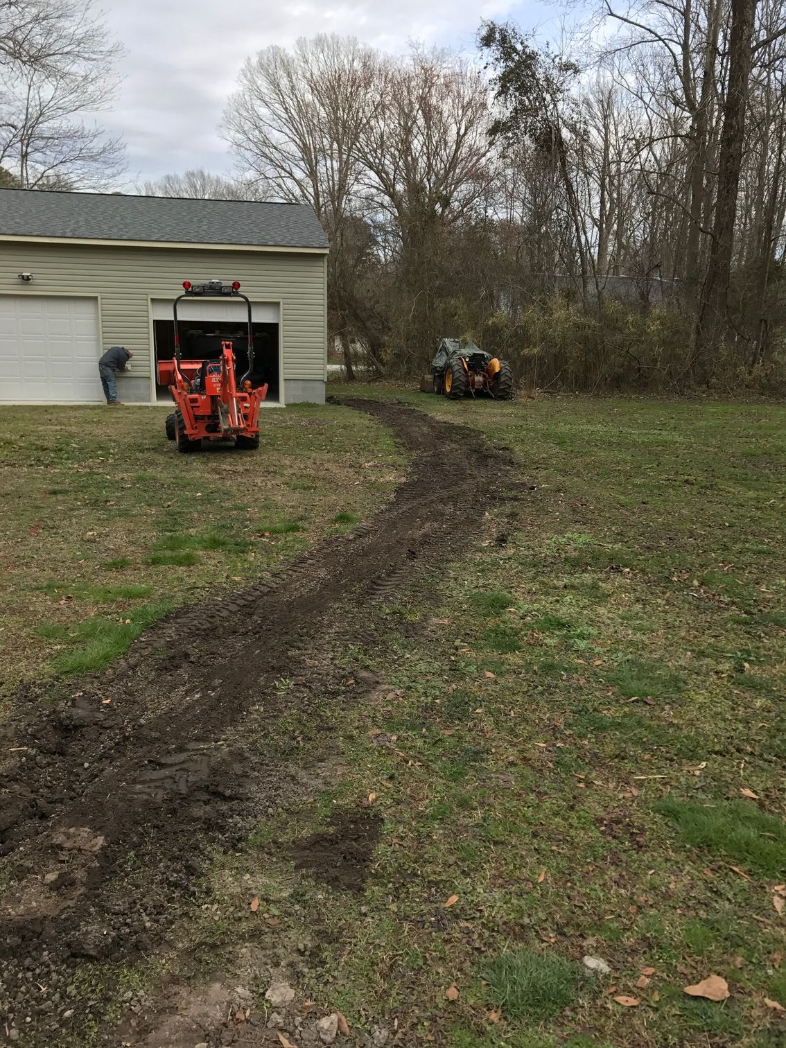 a tractor is digging a hole in the grass in front of a garage 