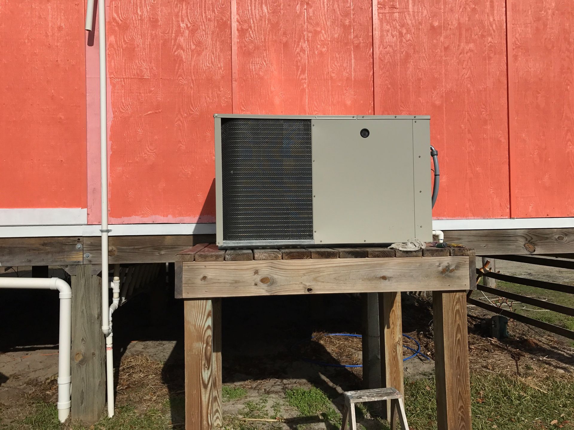an air conditioner is sitting on a wooden platform in front of a red building 