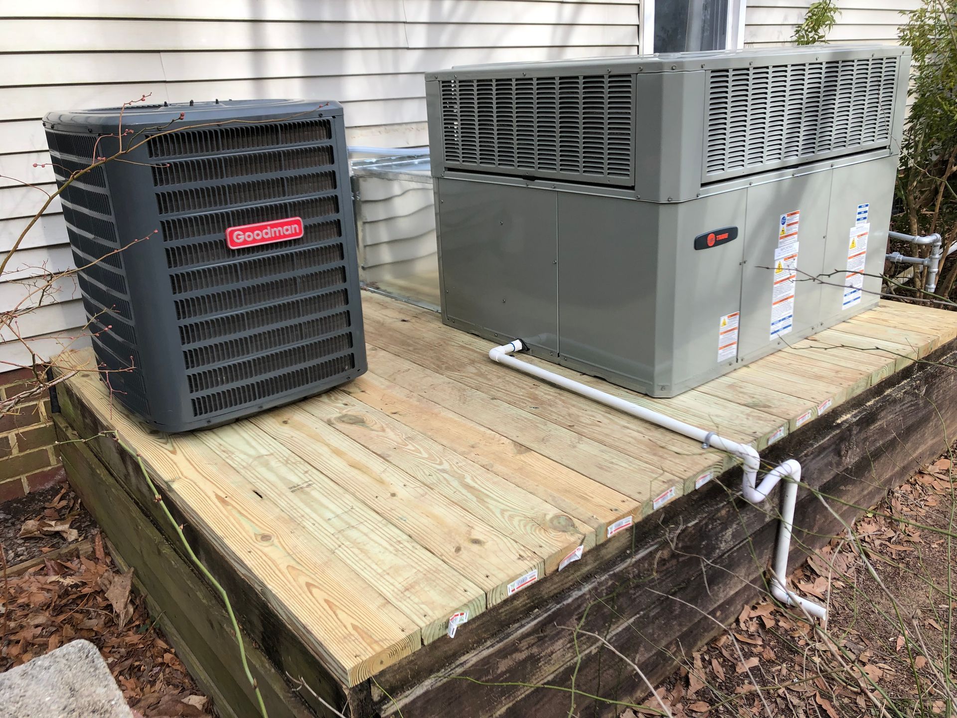 two air conditioners are sitting on a wooden deck next to a house