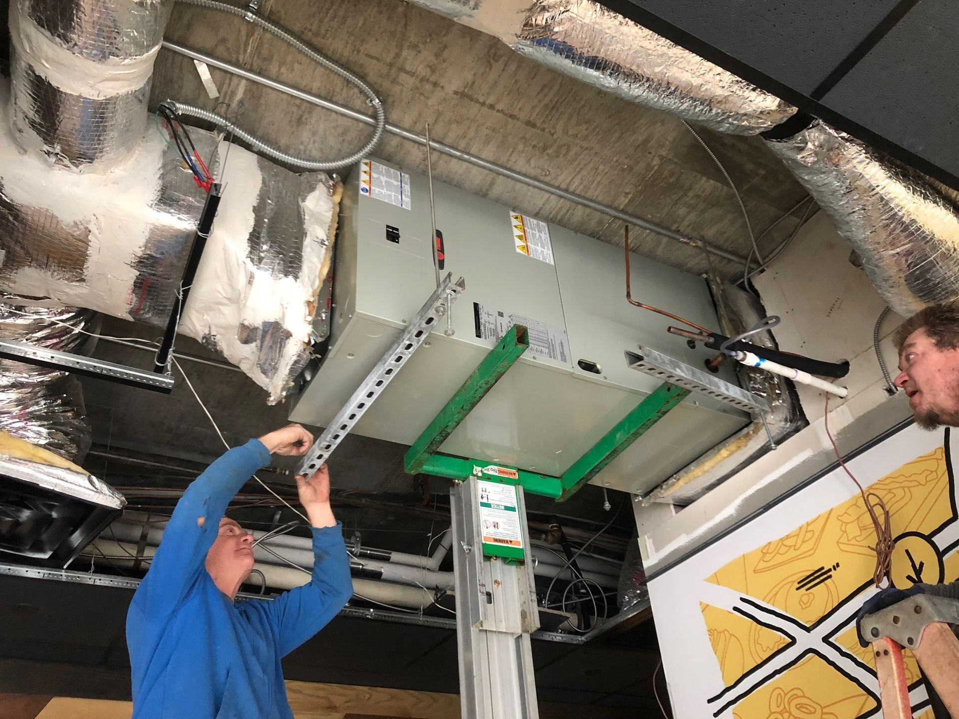 two men are working on a ceiling vent in a building