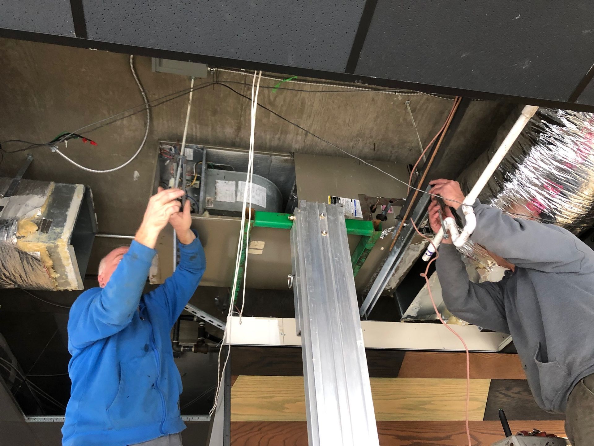 two men are working on a ceiling vent in a building