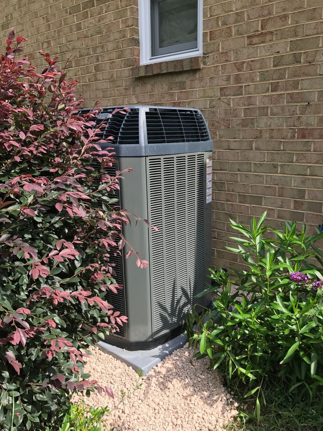 an air conditioner is sitting on the side of a brick building next to a bush 