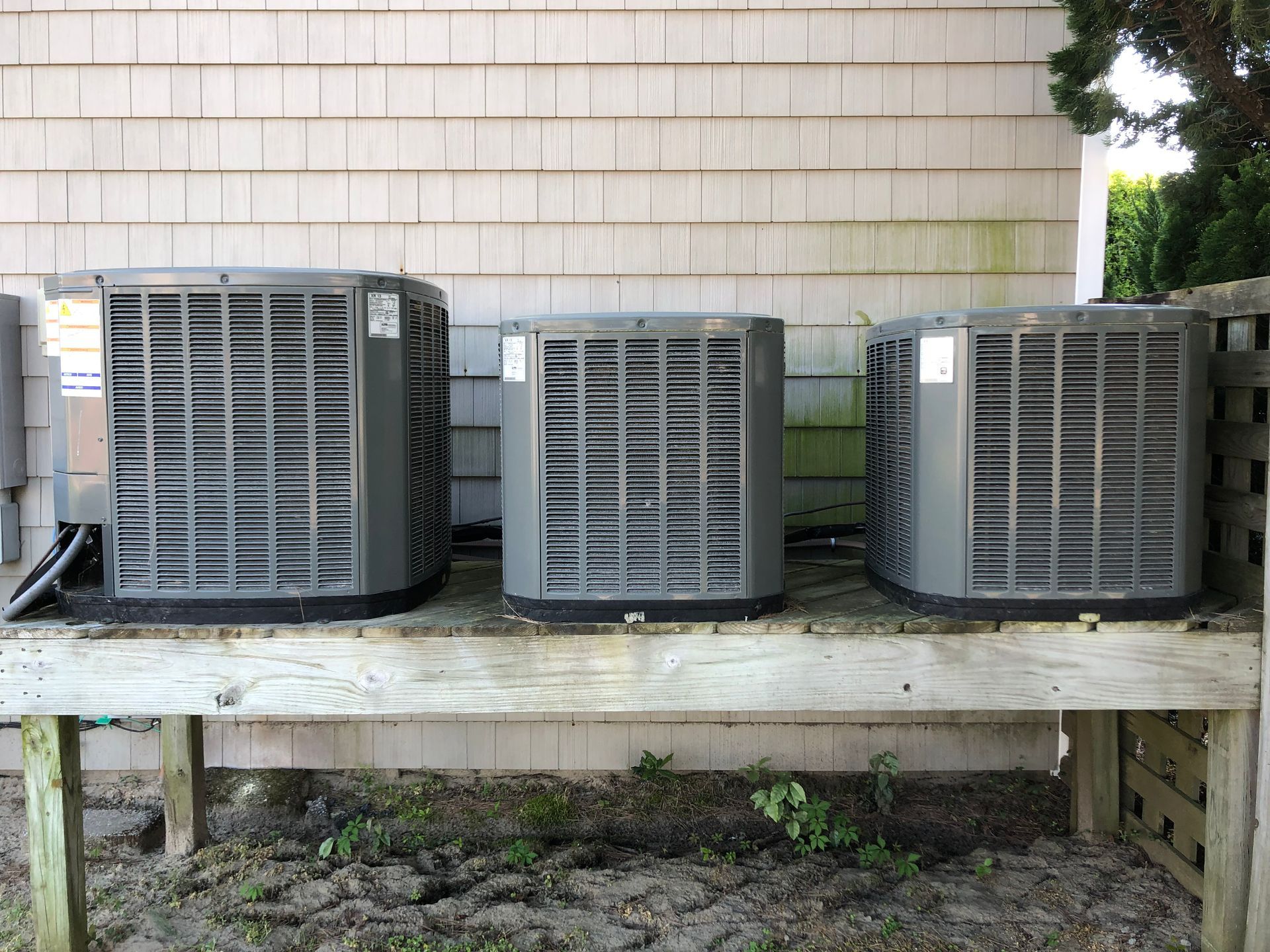 three air conditioners are sitting on a wooden bench outside of a building