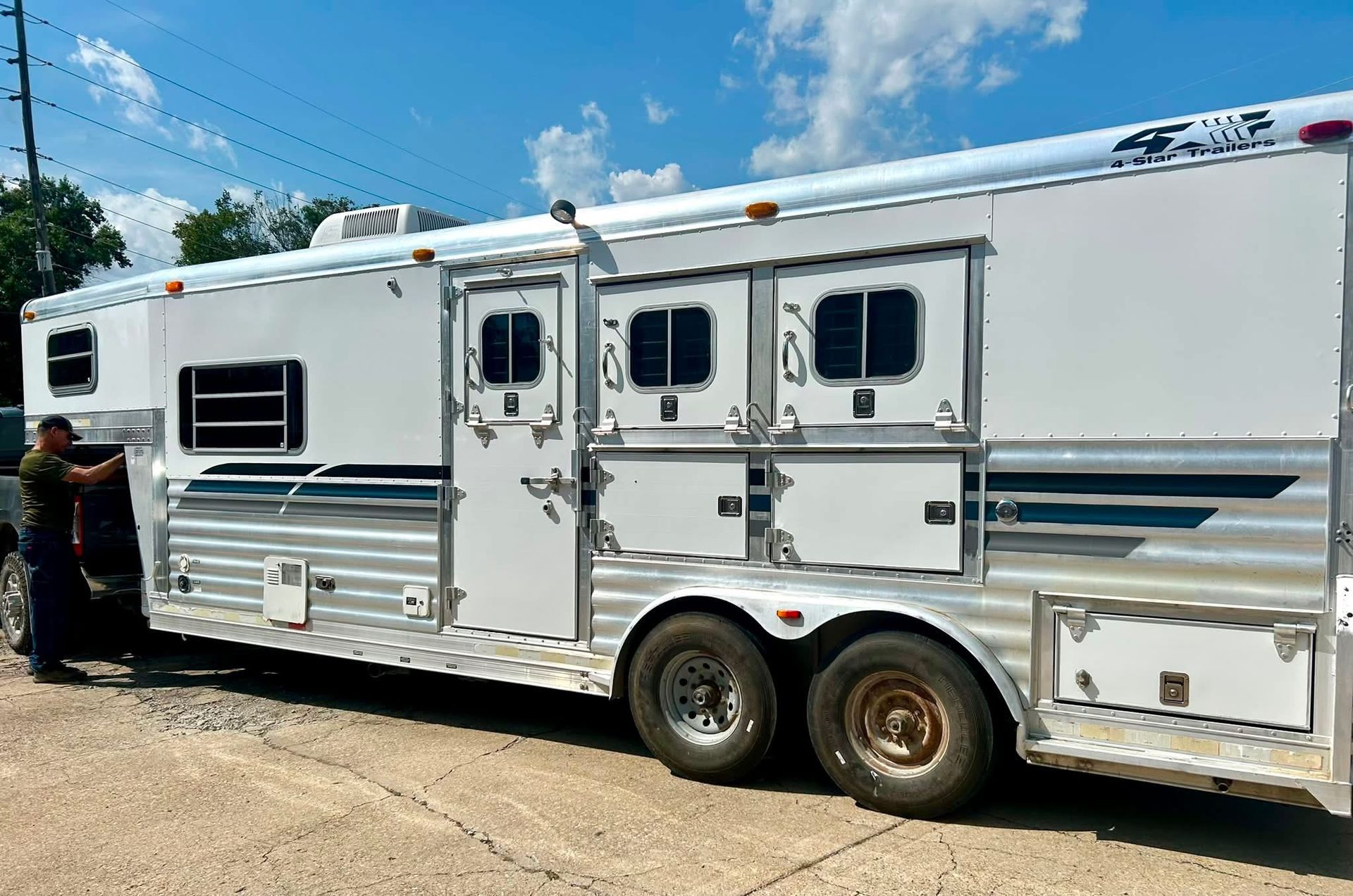 White horse trailer with windows parked on a dirt roadside under a blue sky