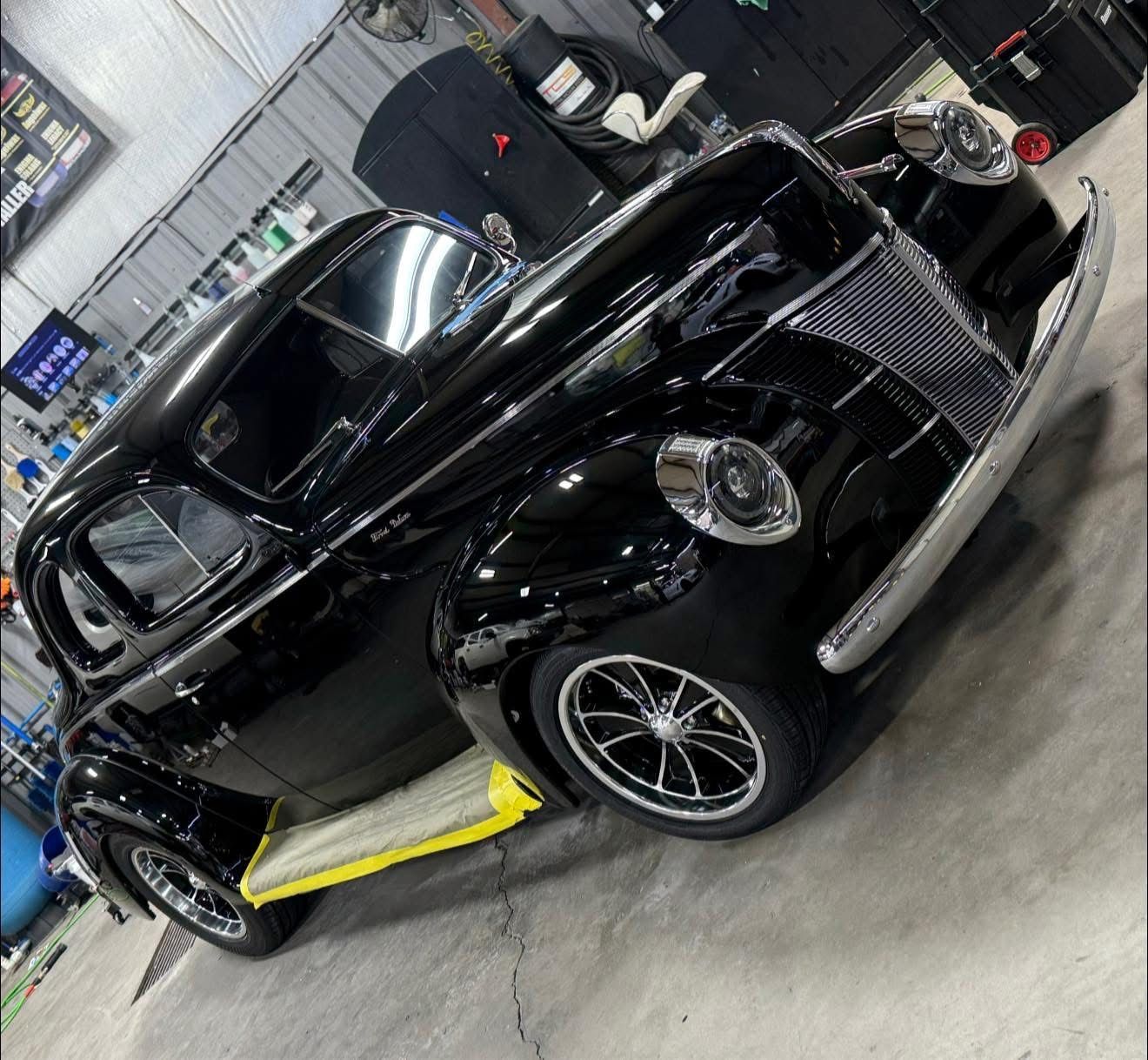 Black classic convertible sports car with yellow side accent in an auto shop garage.