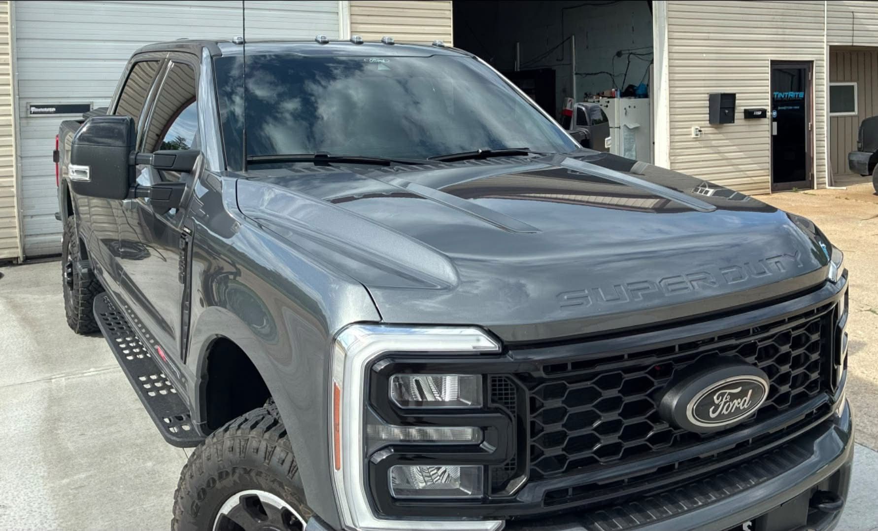 Dark gray Ford pickup truck parked outside a garage with its hood open