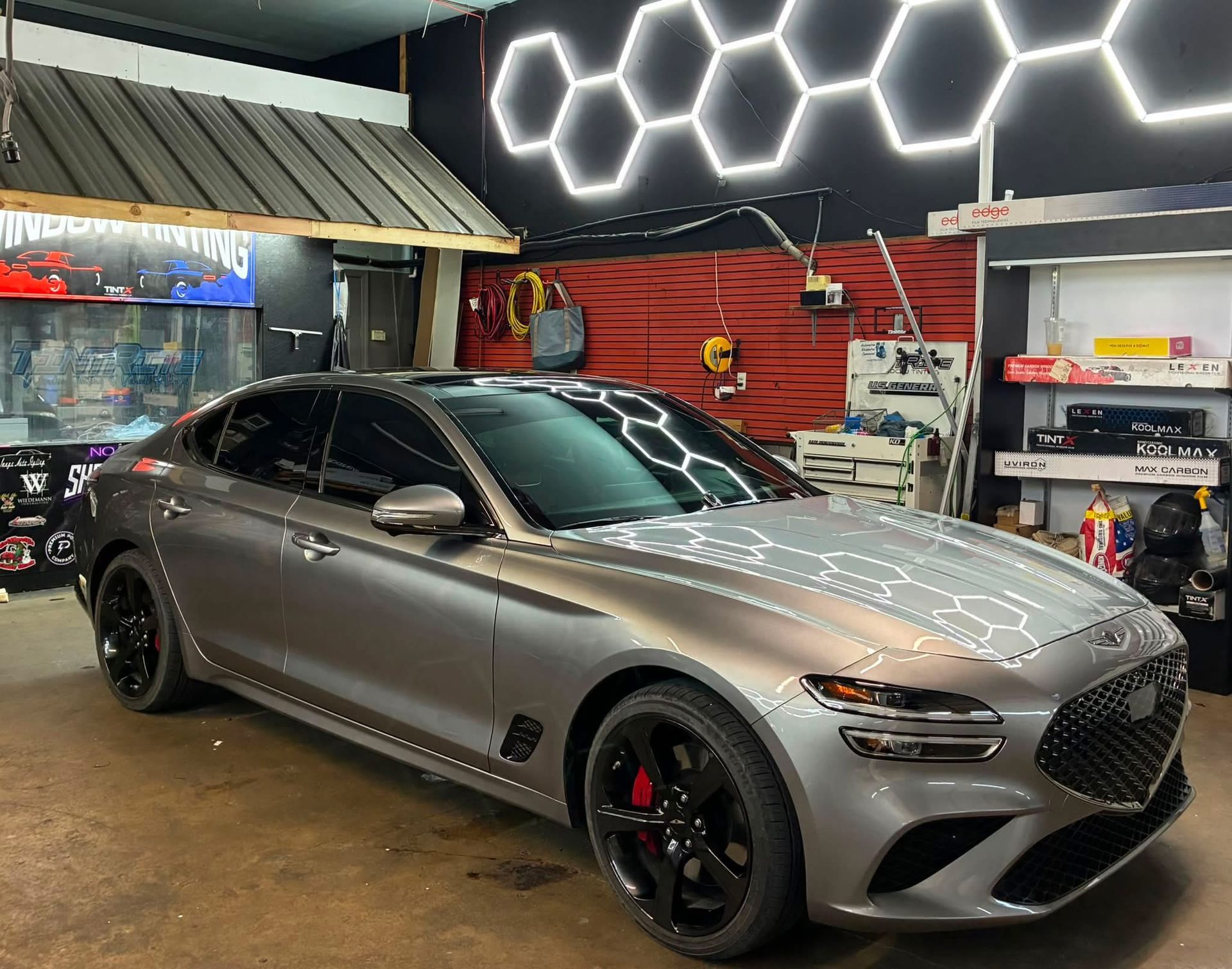 Silver sports sedan parked in a garage with hexagonal lights and red wall decor