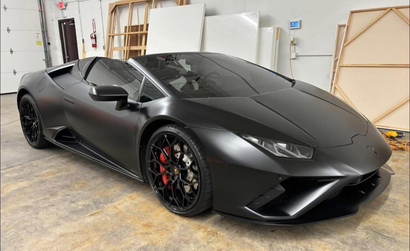 Matte black sports car parked indoors in a garage, front three-quarter view.
