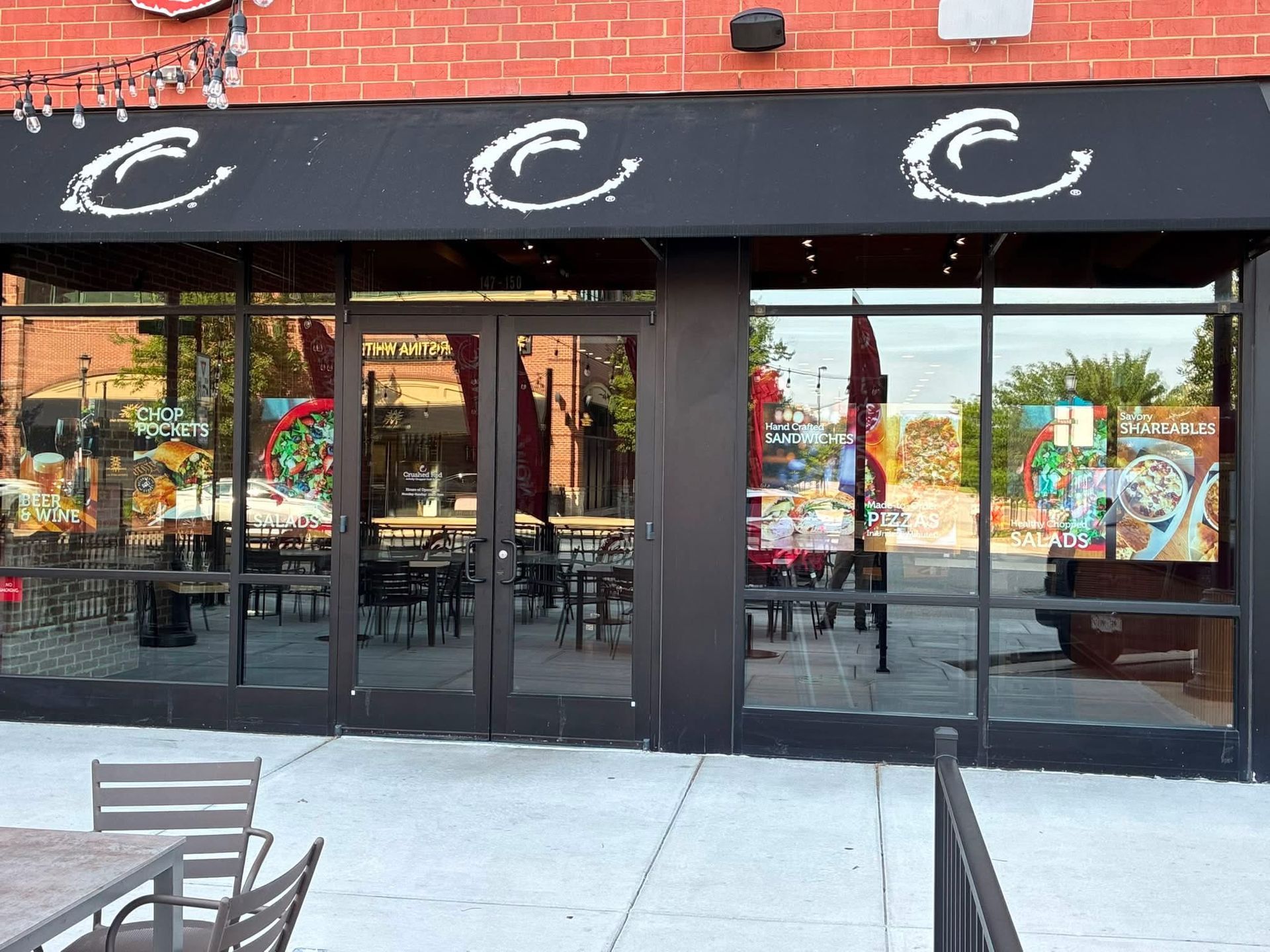 Storefront with black awning and glass doors on a brick building, with outdoor seating in front.