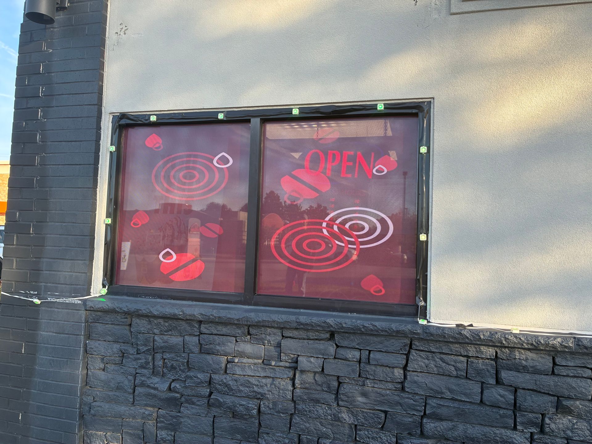 Storefront window with red “OPEN” sign and circular patterns above a dark stone wall