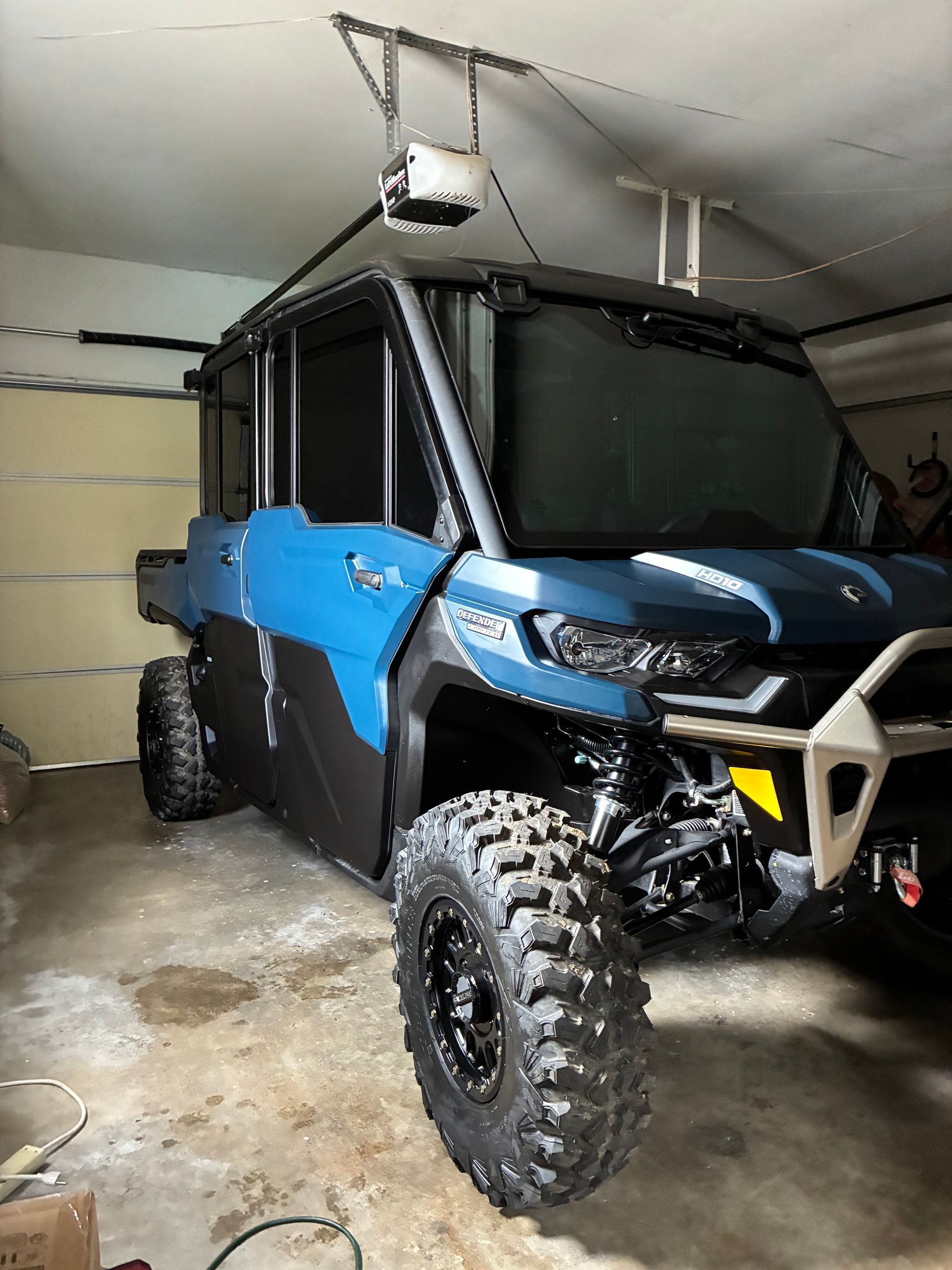 Blue and black off-road UTV parked in a garage, with large tires and roof-mounted equipment