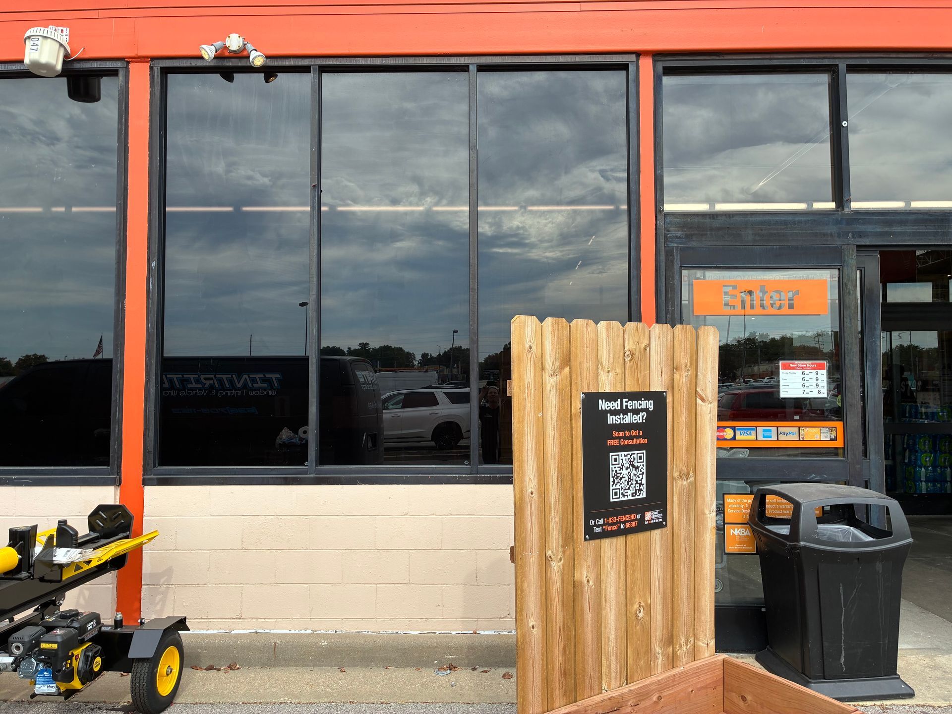 Storefront with dark tinted windows, a wooden signboard, and a trash can outside under an orange awning.