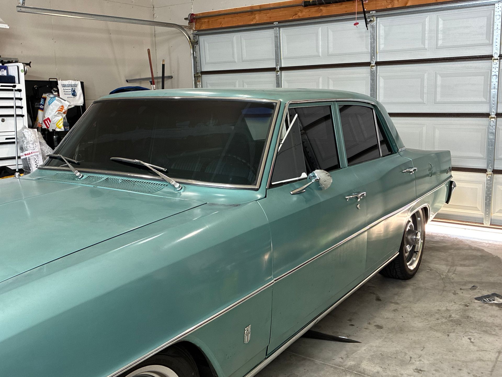 Teal classic sedan parked in a garage with a closed white garage door behind it