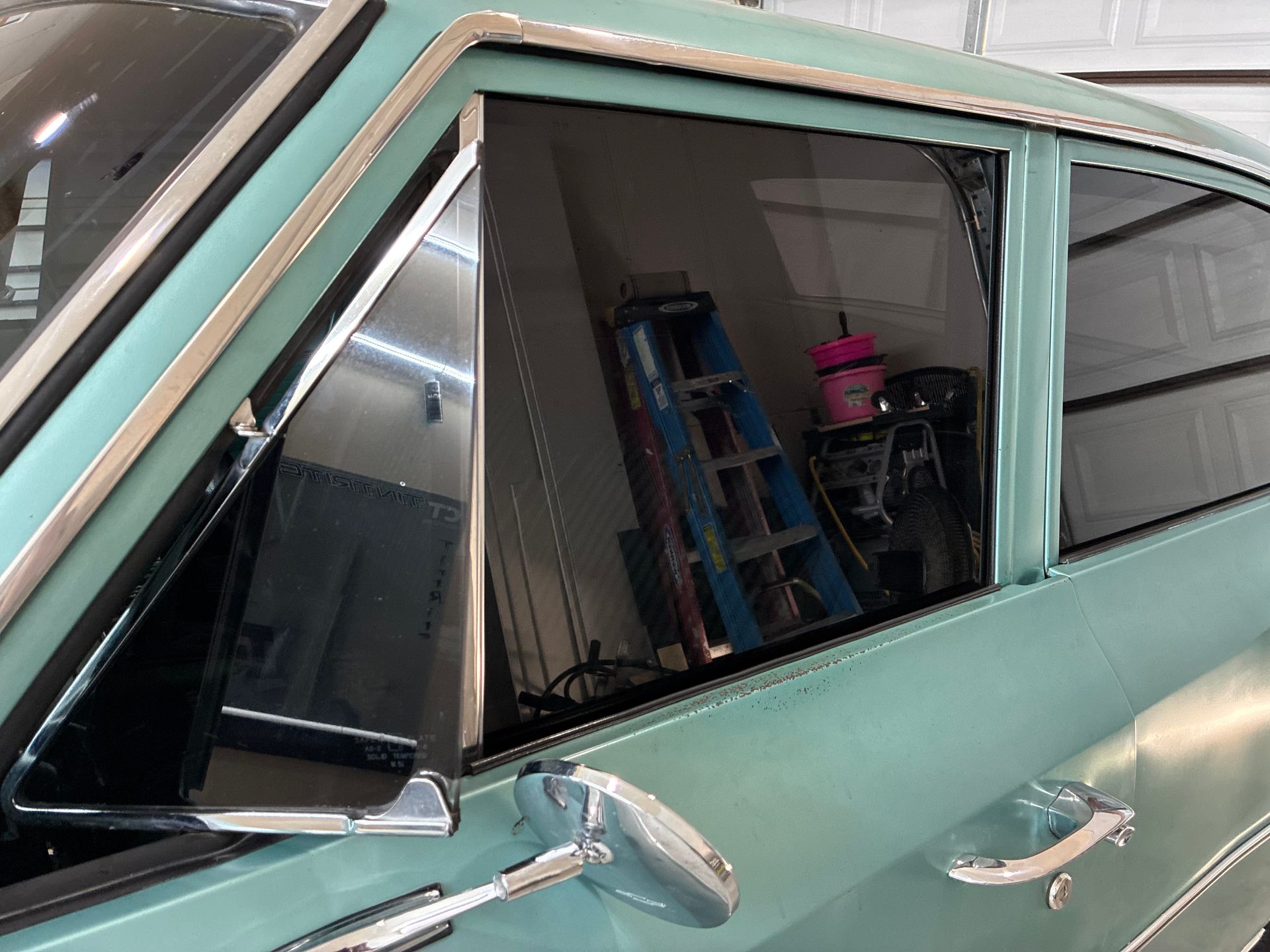 Mint green classic car side windows with chrome trim and mirror in a garage