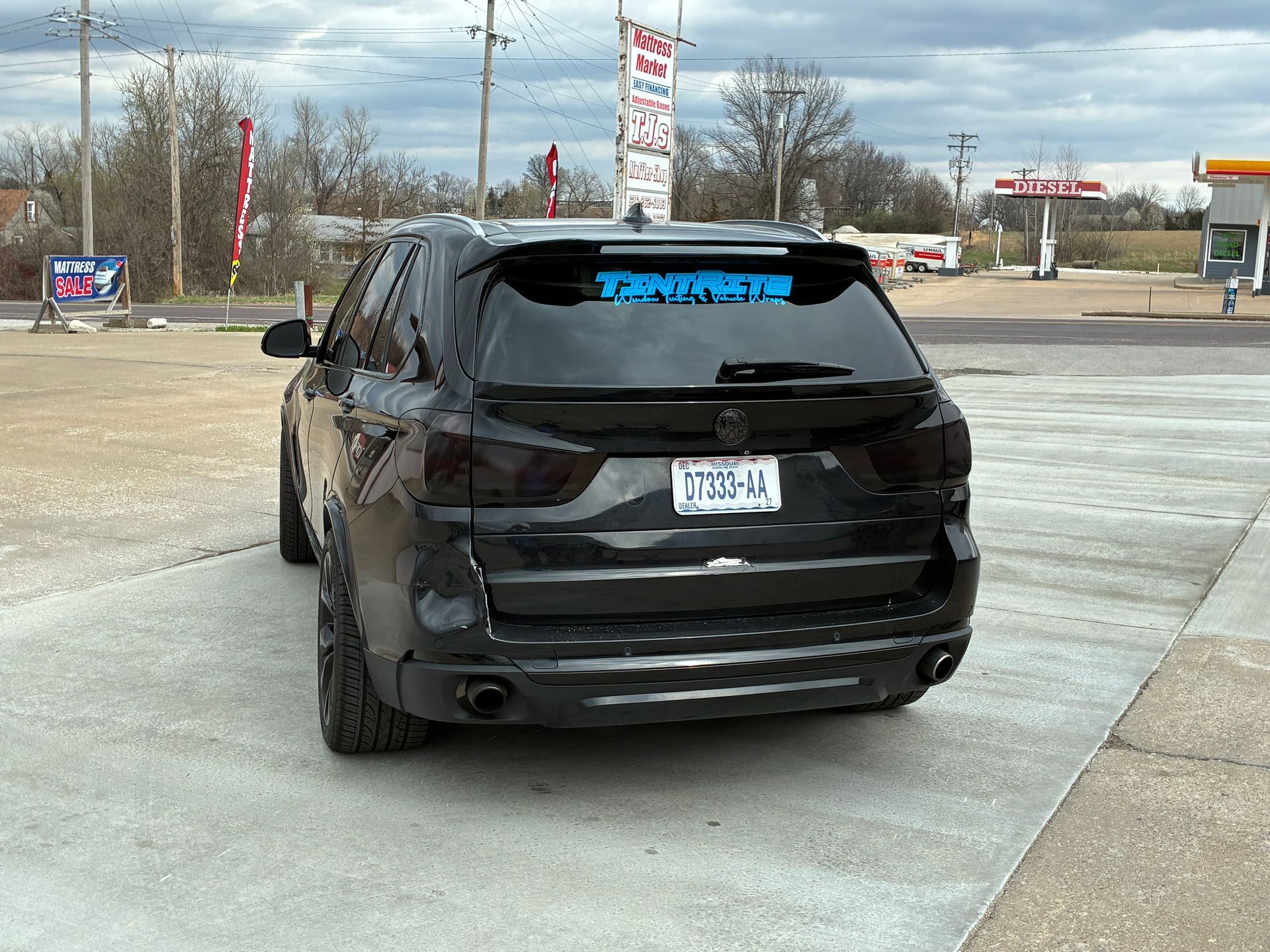 Black SUV parked in a lot, rear view, with a blue banner on the back window.
