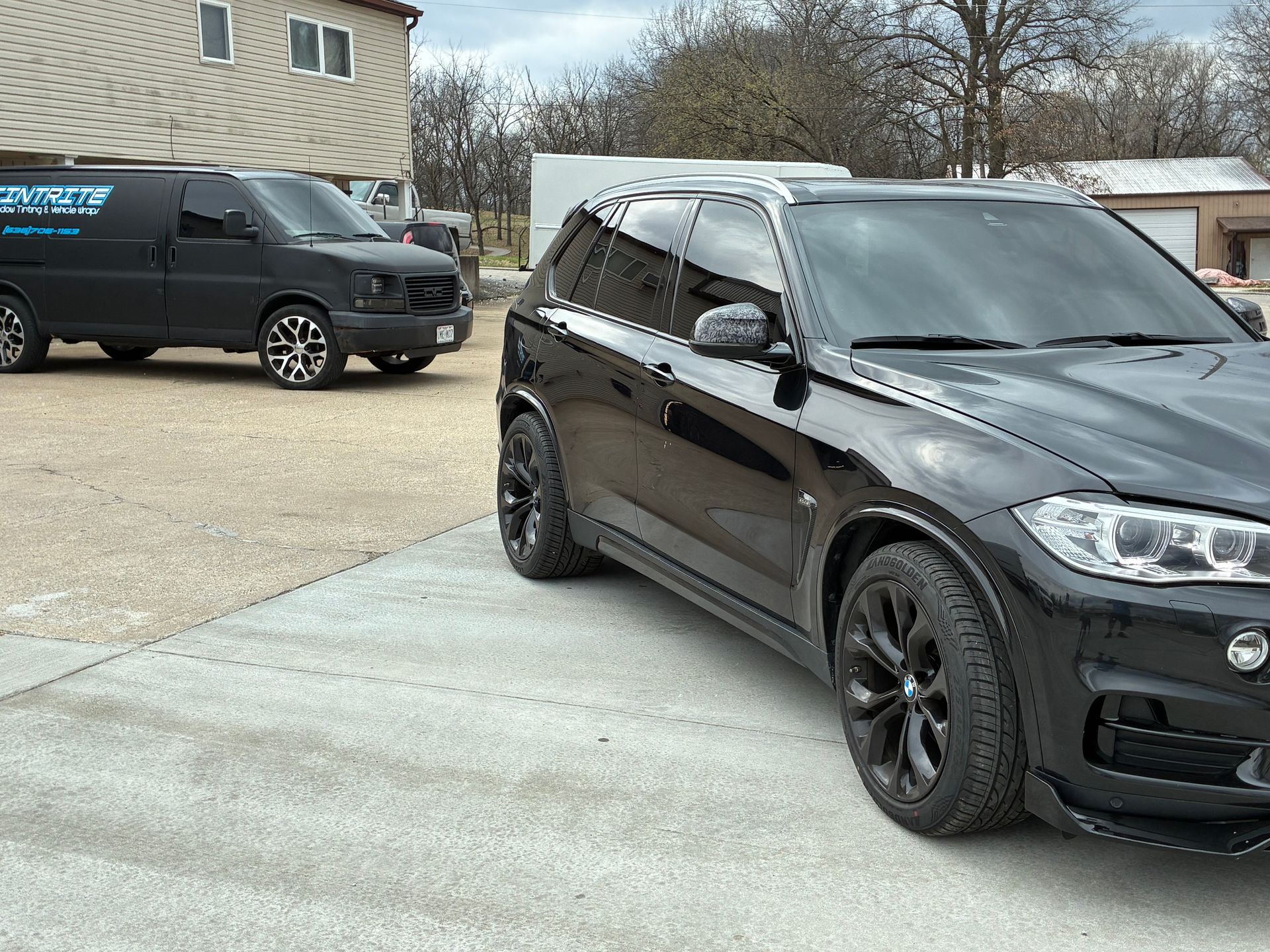 Black SUV parked in a driveway beside a dark work van on a residential street