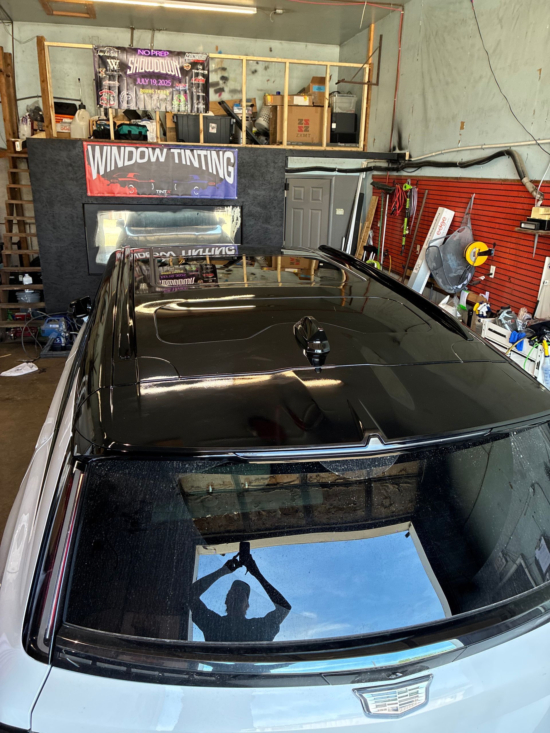Black SUV inside a window tinting shop, viewed from above with tools and signage in the background