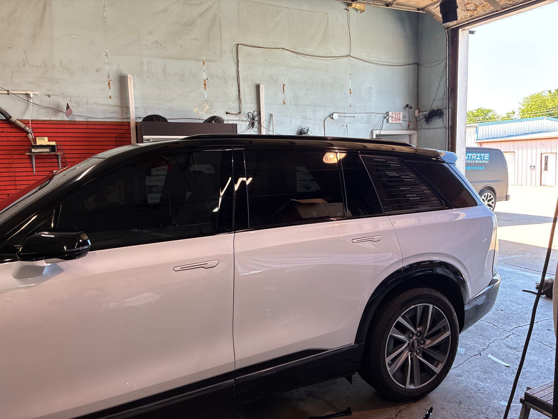 White SUV parked inside a garage with a red wall and open bay door showing daylight outside