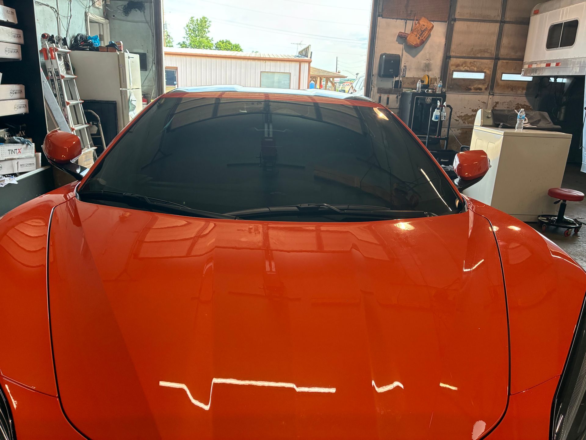Bright orange sports car parked inside a garage, viewed from the front.