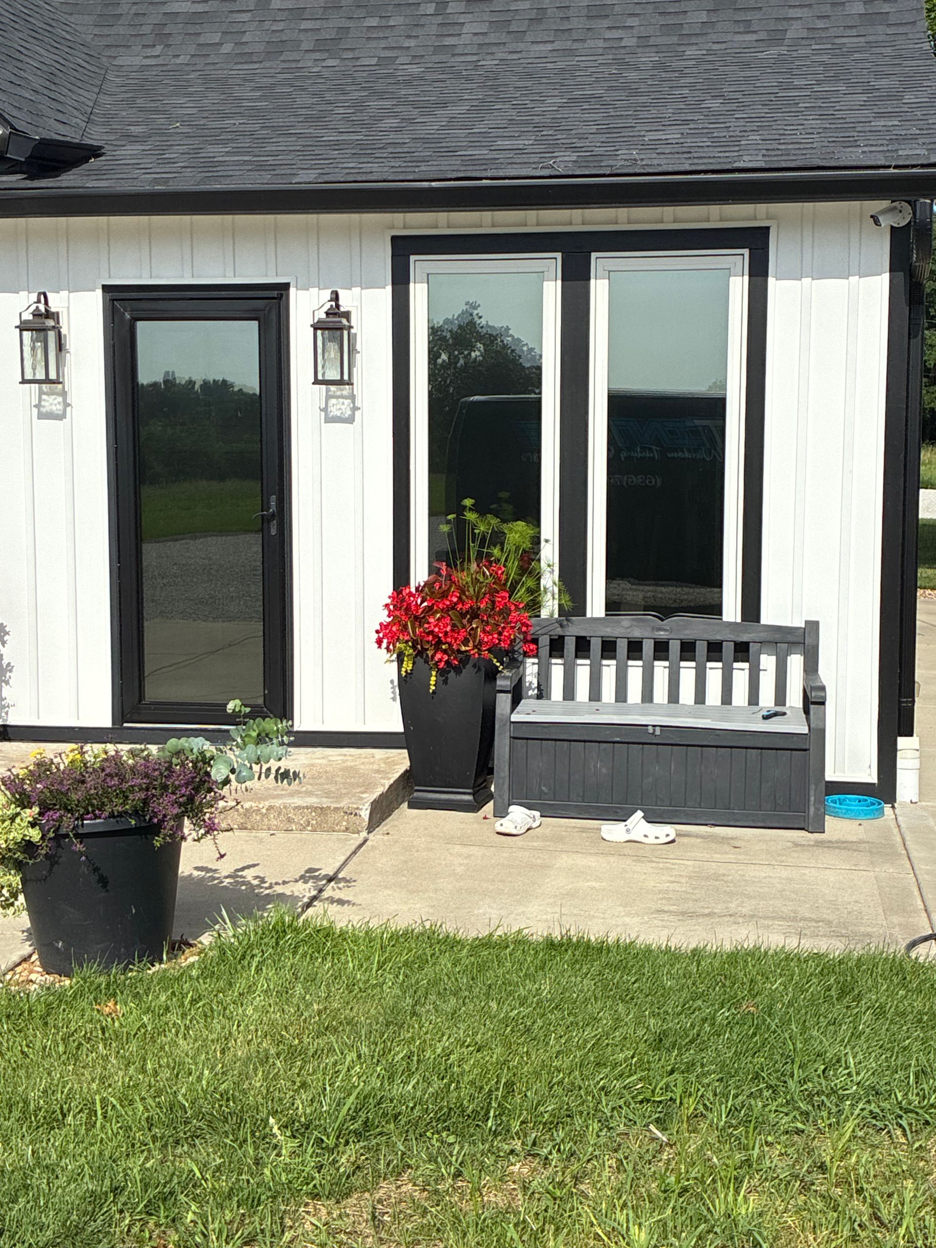Front porch with white siding, dark doors, potted flowers, bench, and green lawn.