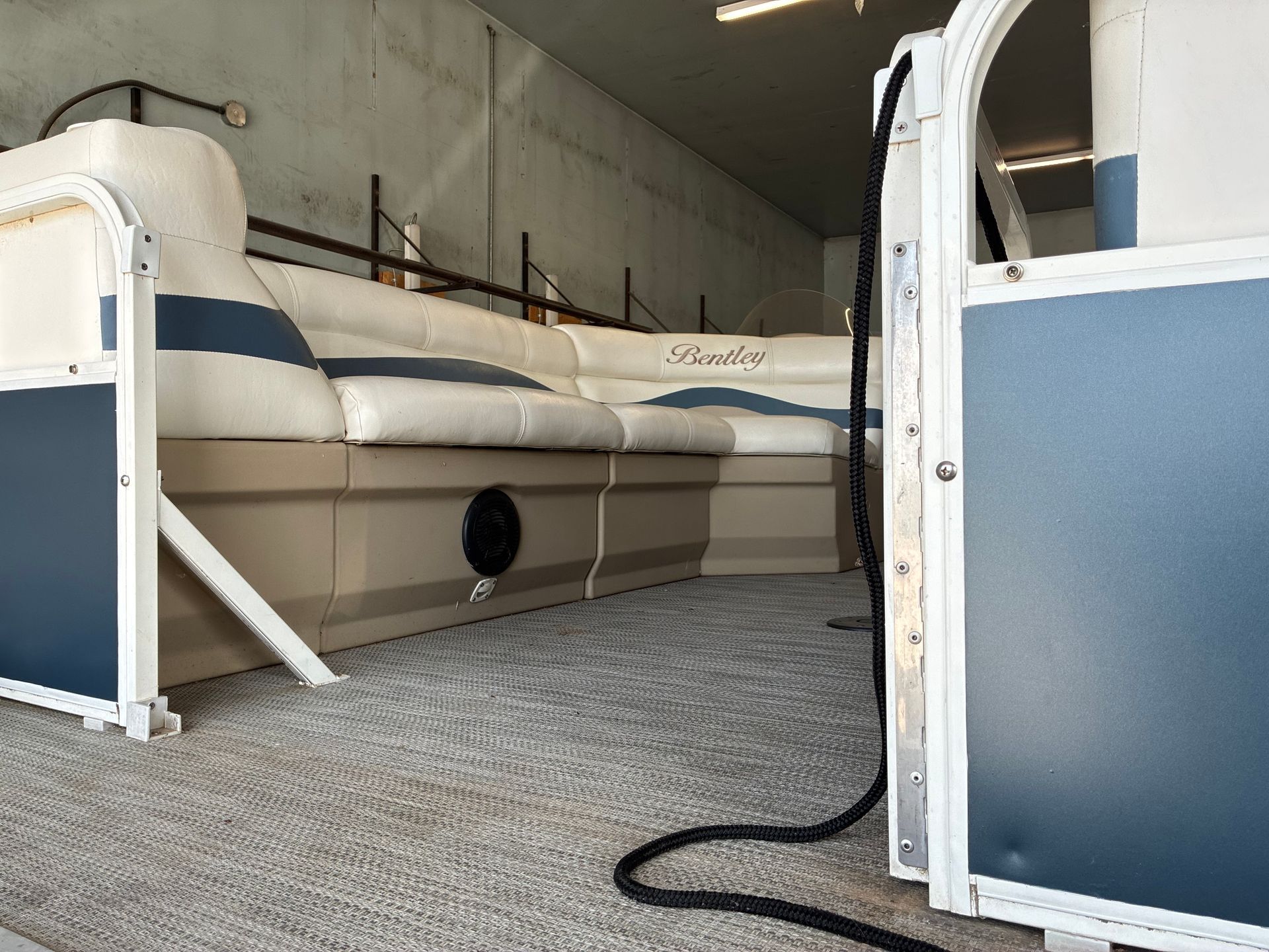 Blue-and-white pontoon boat stored indoors on carpeted floor, viewed from the side.