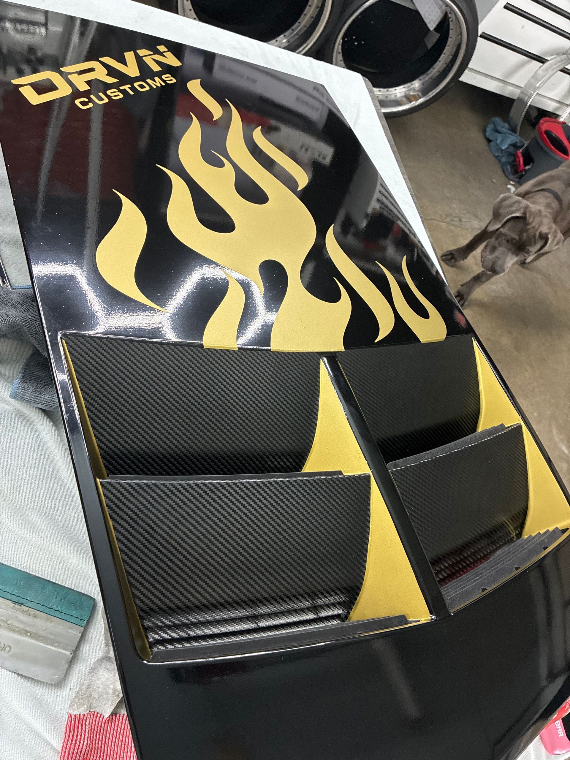 Black and yellow custom car hood with flame decal and carbon-fiber-style panels on a vehicle or display stand