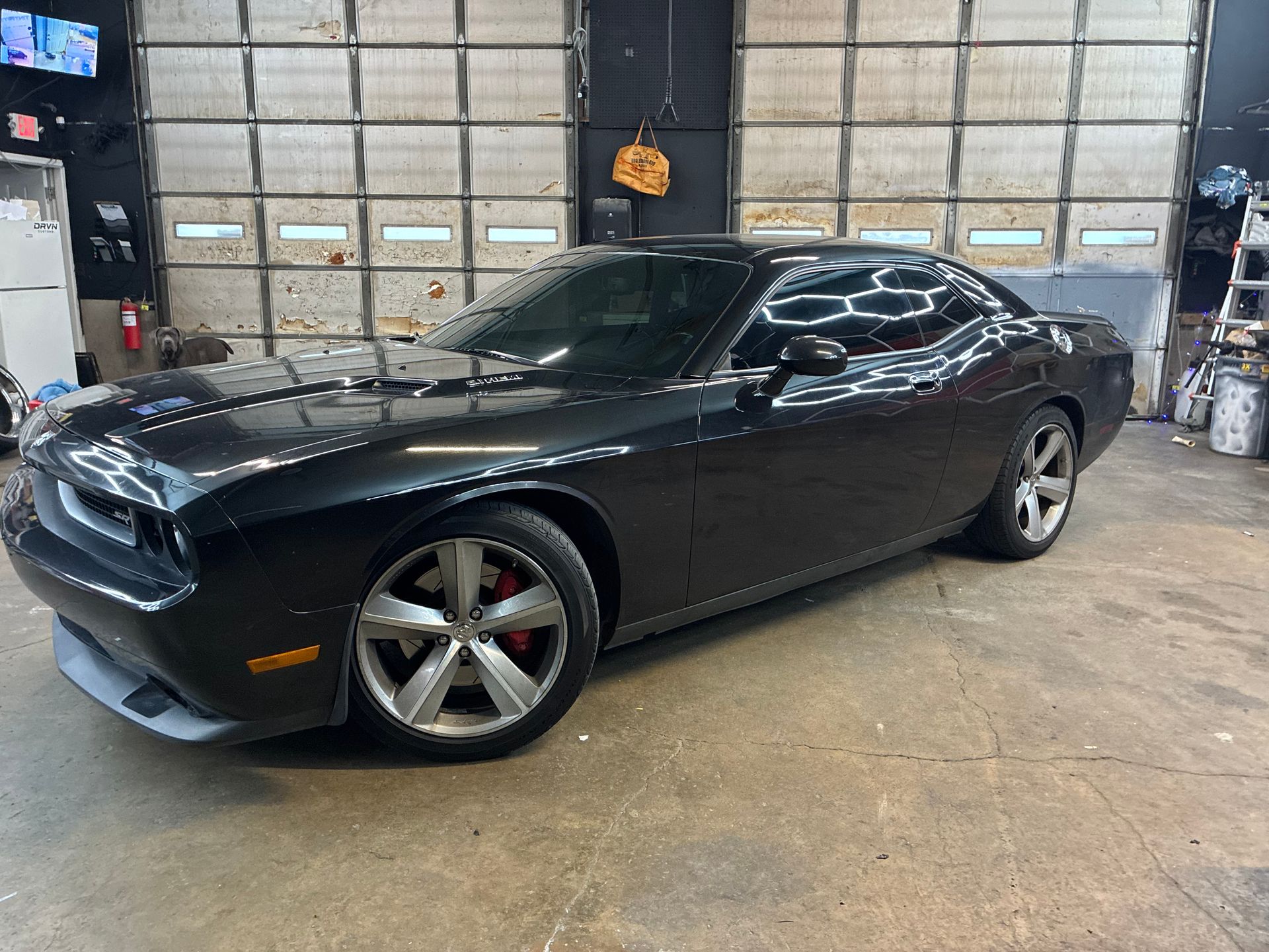 Black Dodge Challenger parked inside an auto garage, viewed from the front-left side