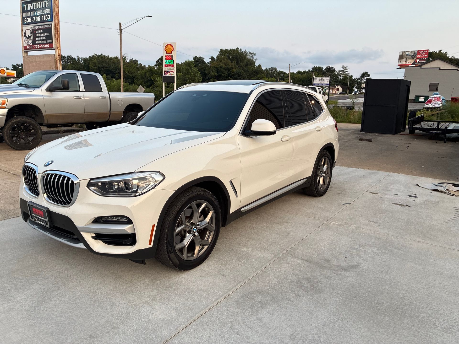 White BMW SUV parked at a gas station, front-left view on a concrete lot.