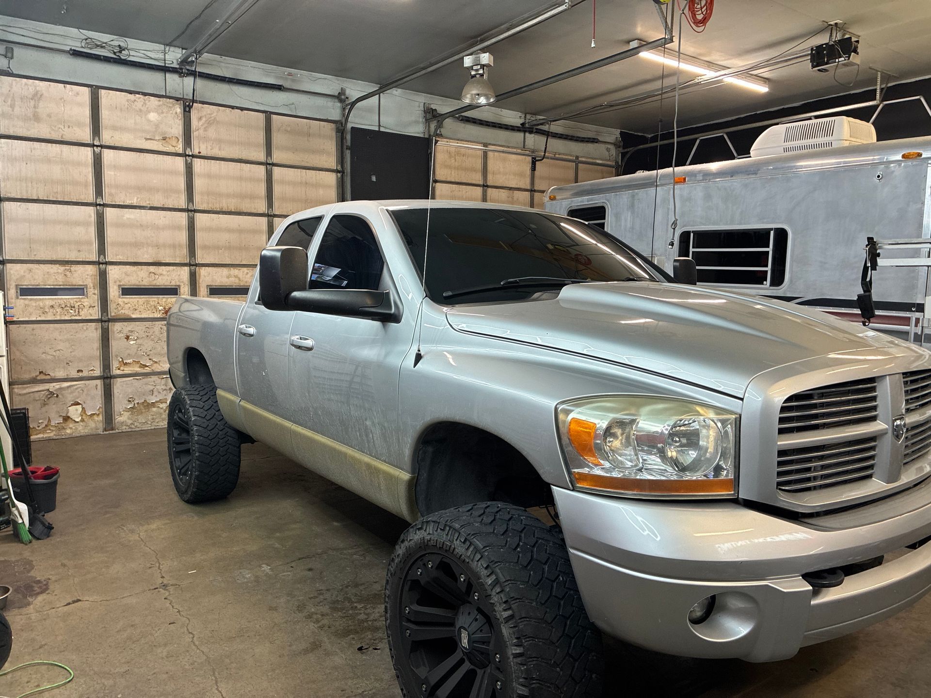 Lifted silver pickup truck parked inside a garage with a raised suspension and large off-road tires