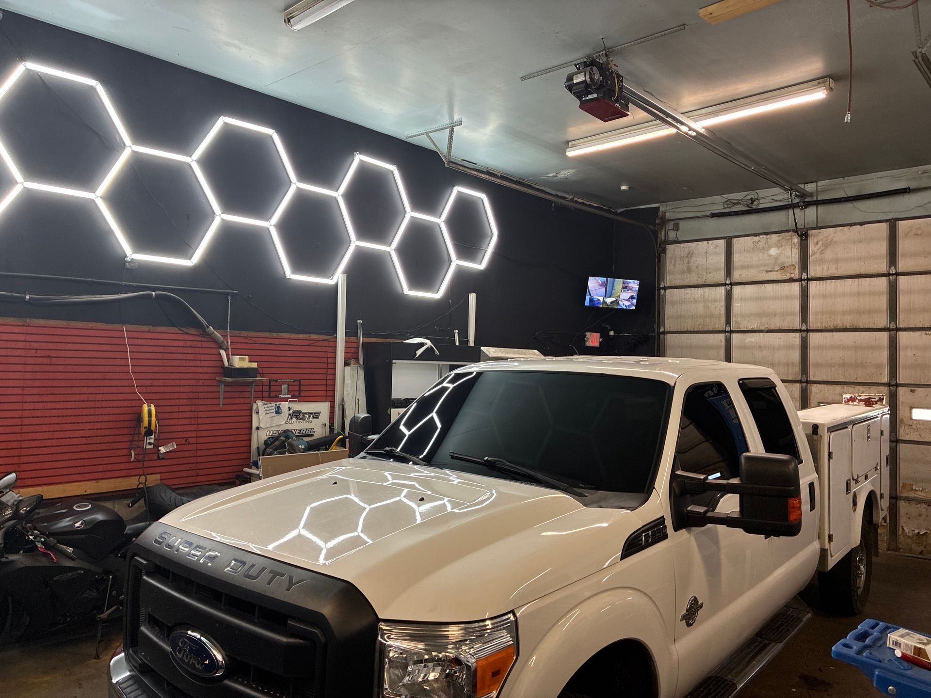 White pickup truck in a garage with bright hexagonal wall lights and tools in the background