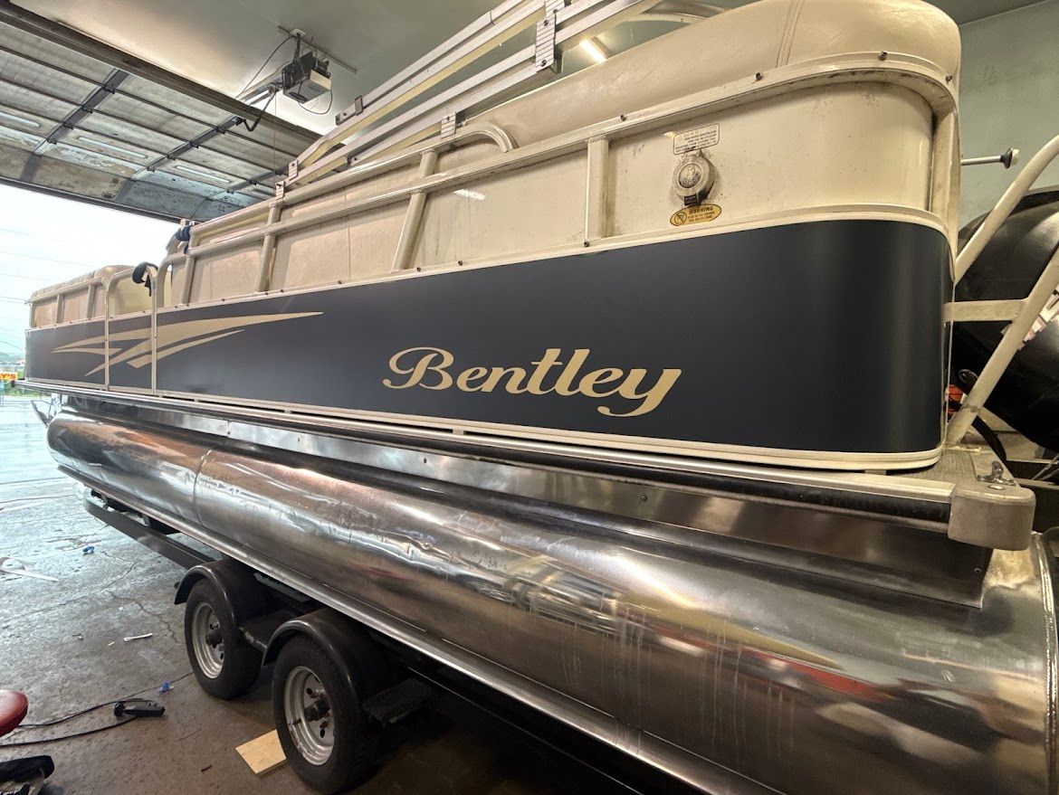 Bentley pontoon boat on a trailer inside a warehouse, cream and navy with polished aluminum trim