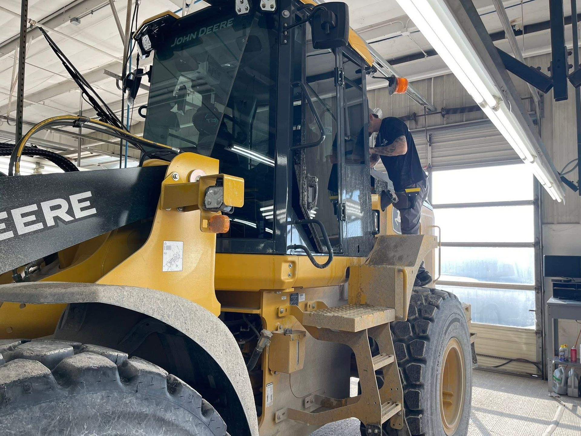 Yellow John Deere loader in a workshop, with a person standing on the cab steps.
