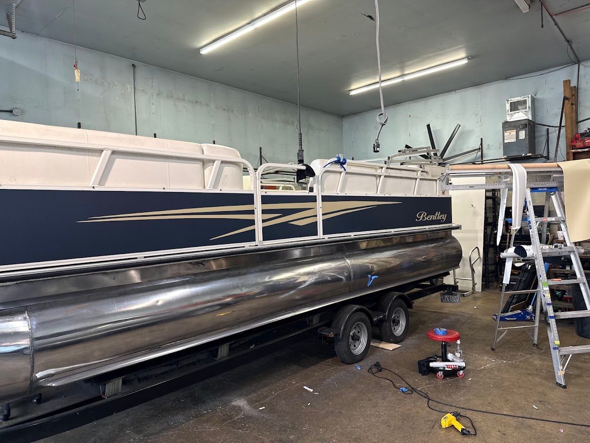Workshop with a black inflatable boat on a trailer, ladders, and tools in a garage.