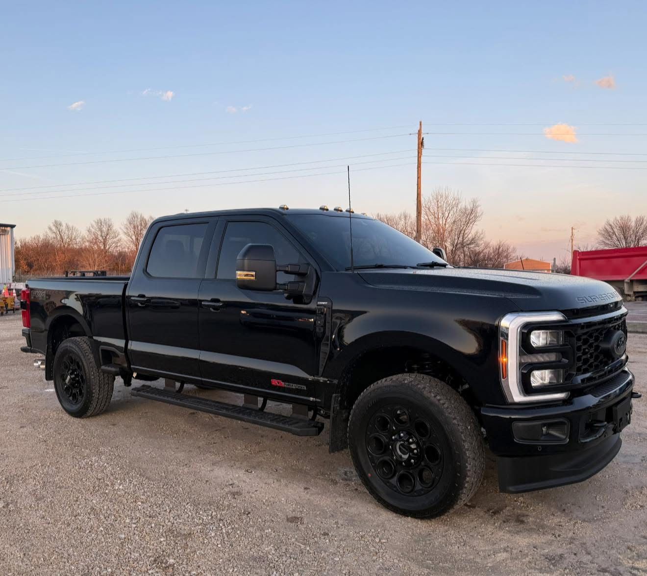 Black lifted pickup truck parked on gravel at dusk, with a sunset sky in the background