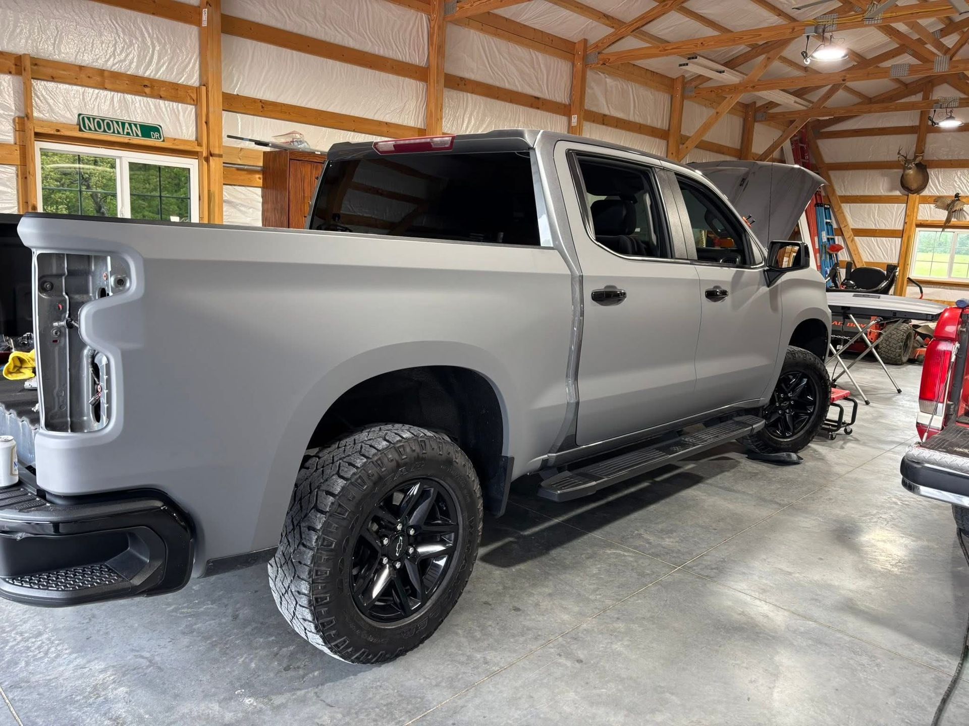 Gray pickup truck in a wooden garage, shown from the rear side with black wheels.