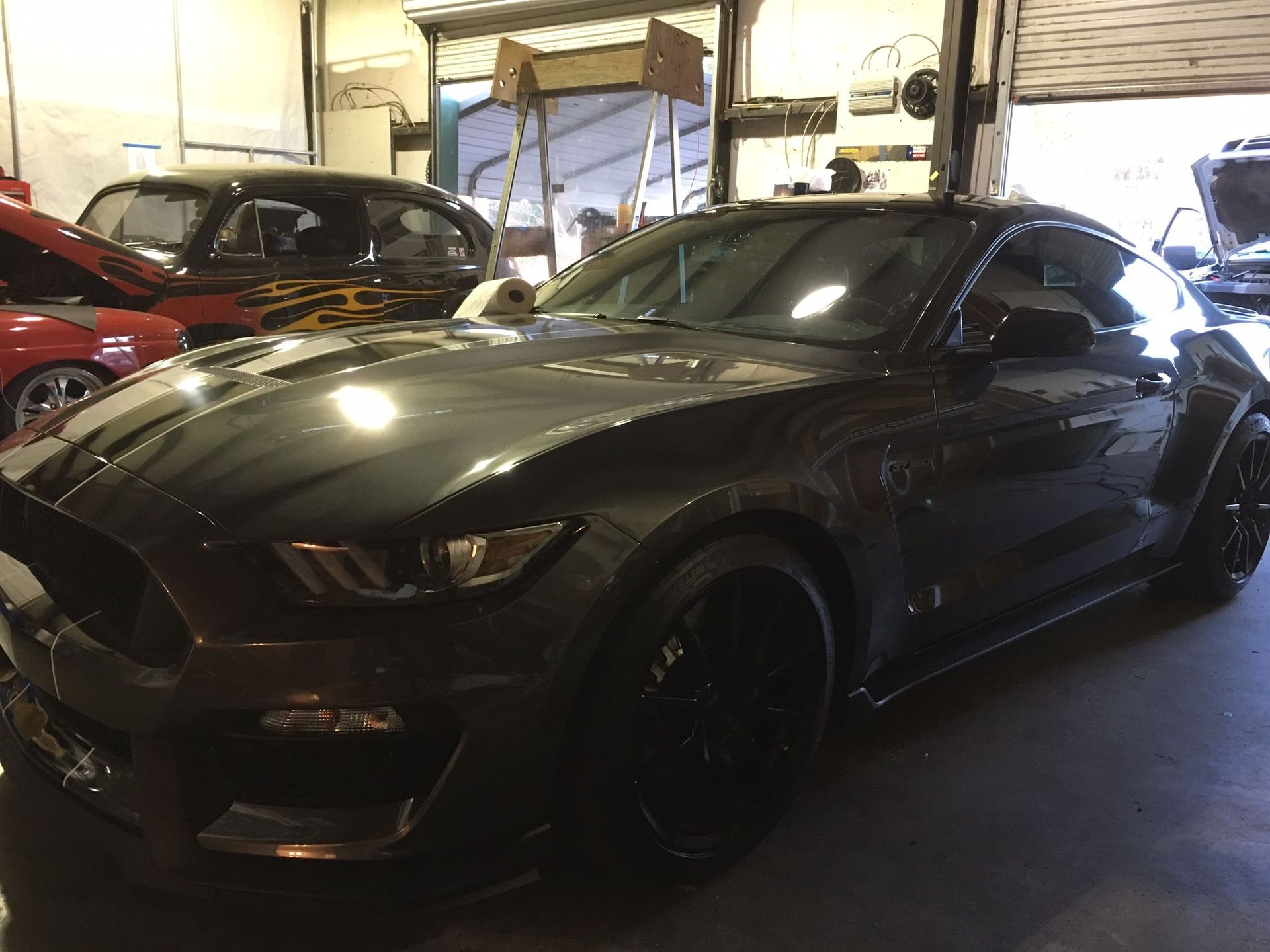 A gray mustang is parked in a garage next to other cars.