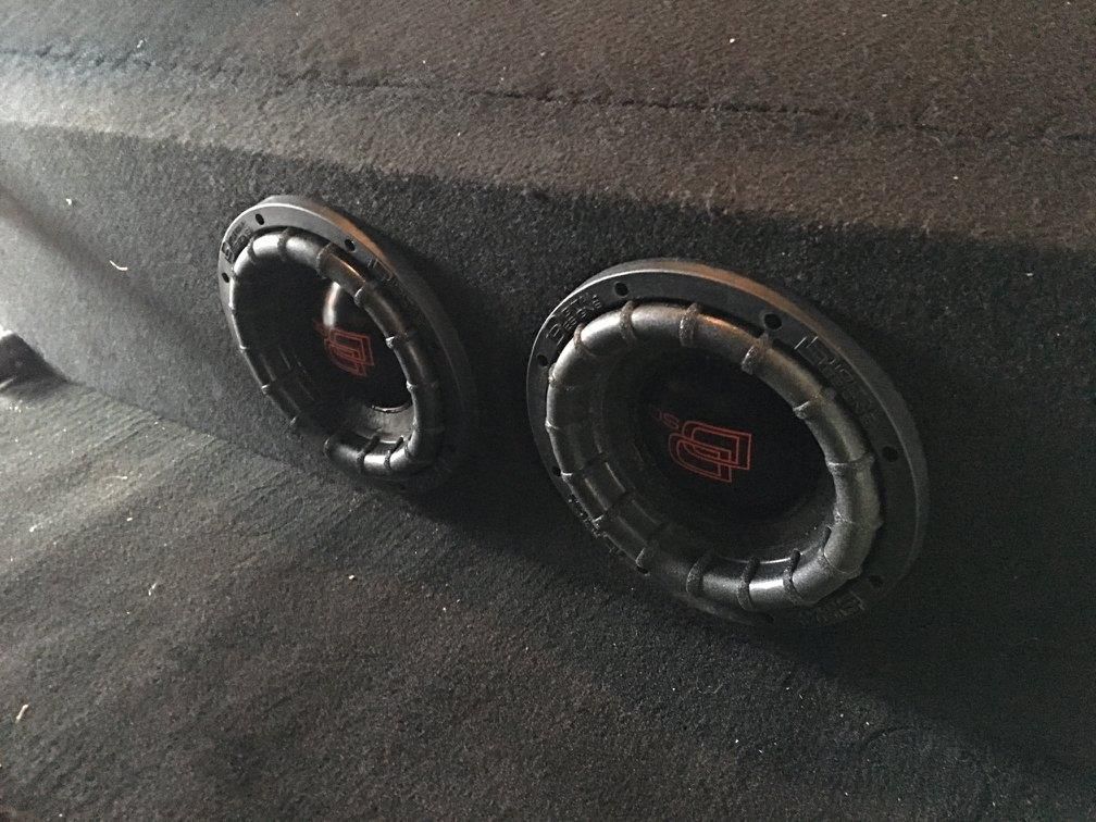 Two subwoofers are sitting in a box on the floor.