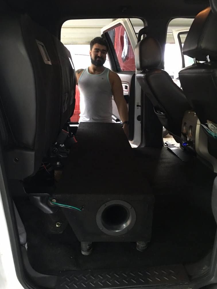 A man is standing in the back of a car next to a subwoofer.