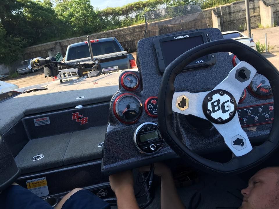 A man is sitting in a boat with a steering wheel that says bc on it.