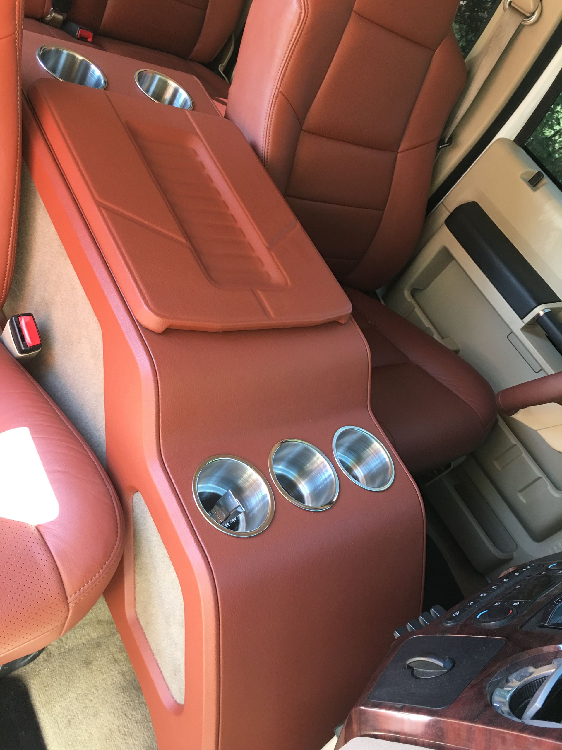 A brown leather arm rest in a car with four cup holders