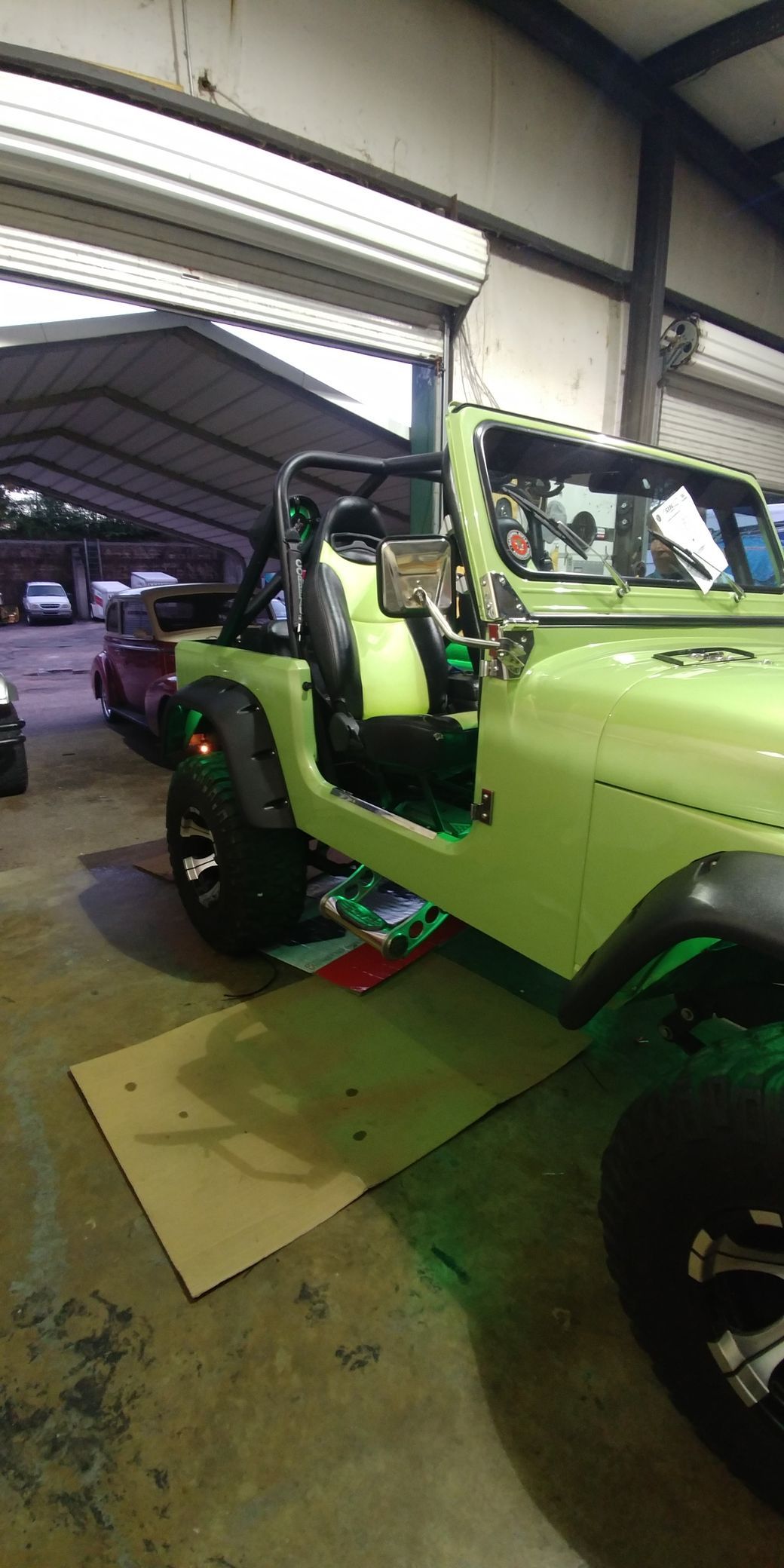 A green jeep is parked in a garage with its doors open.