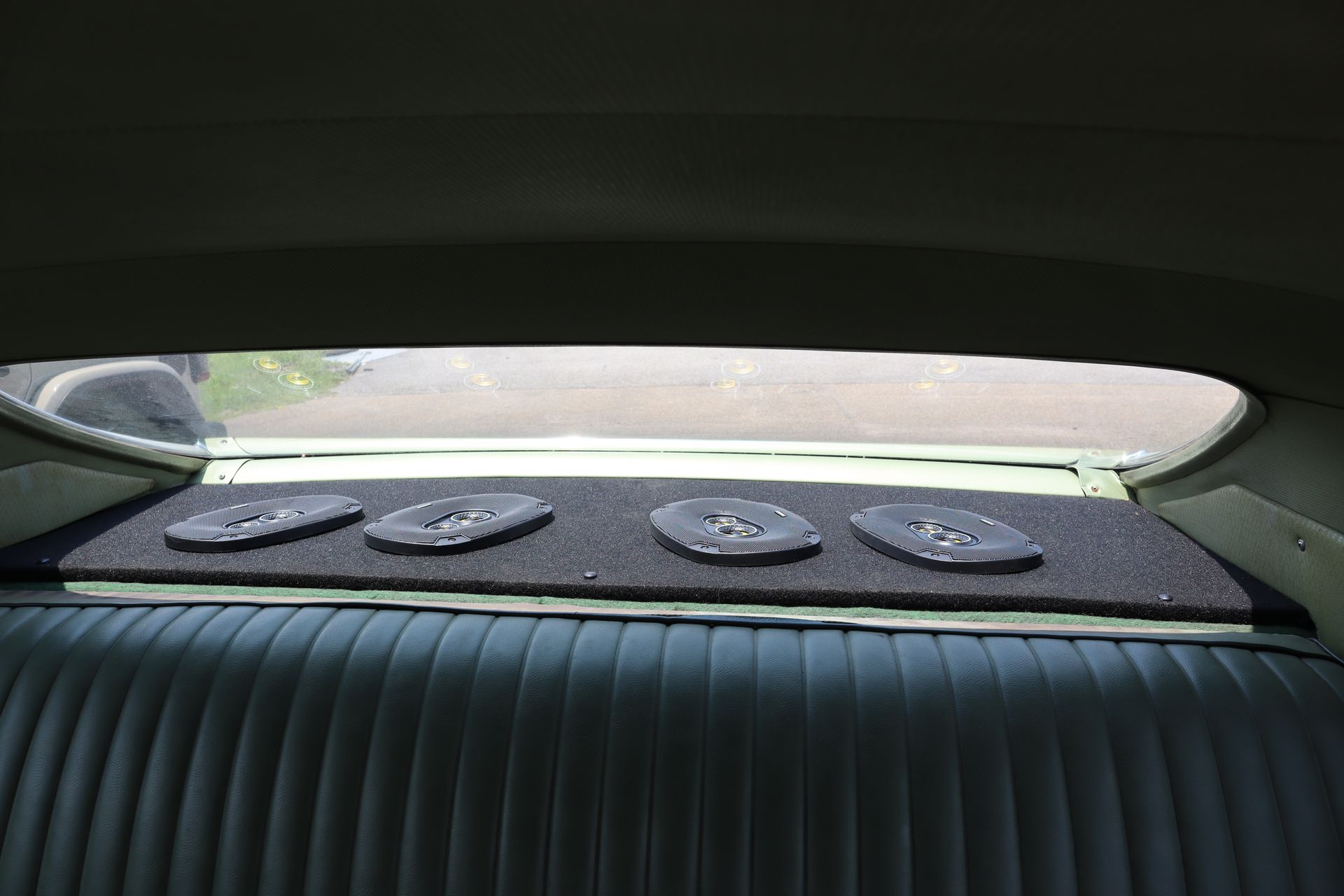 The back seat of a car has a shelf with four speakers on it.