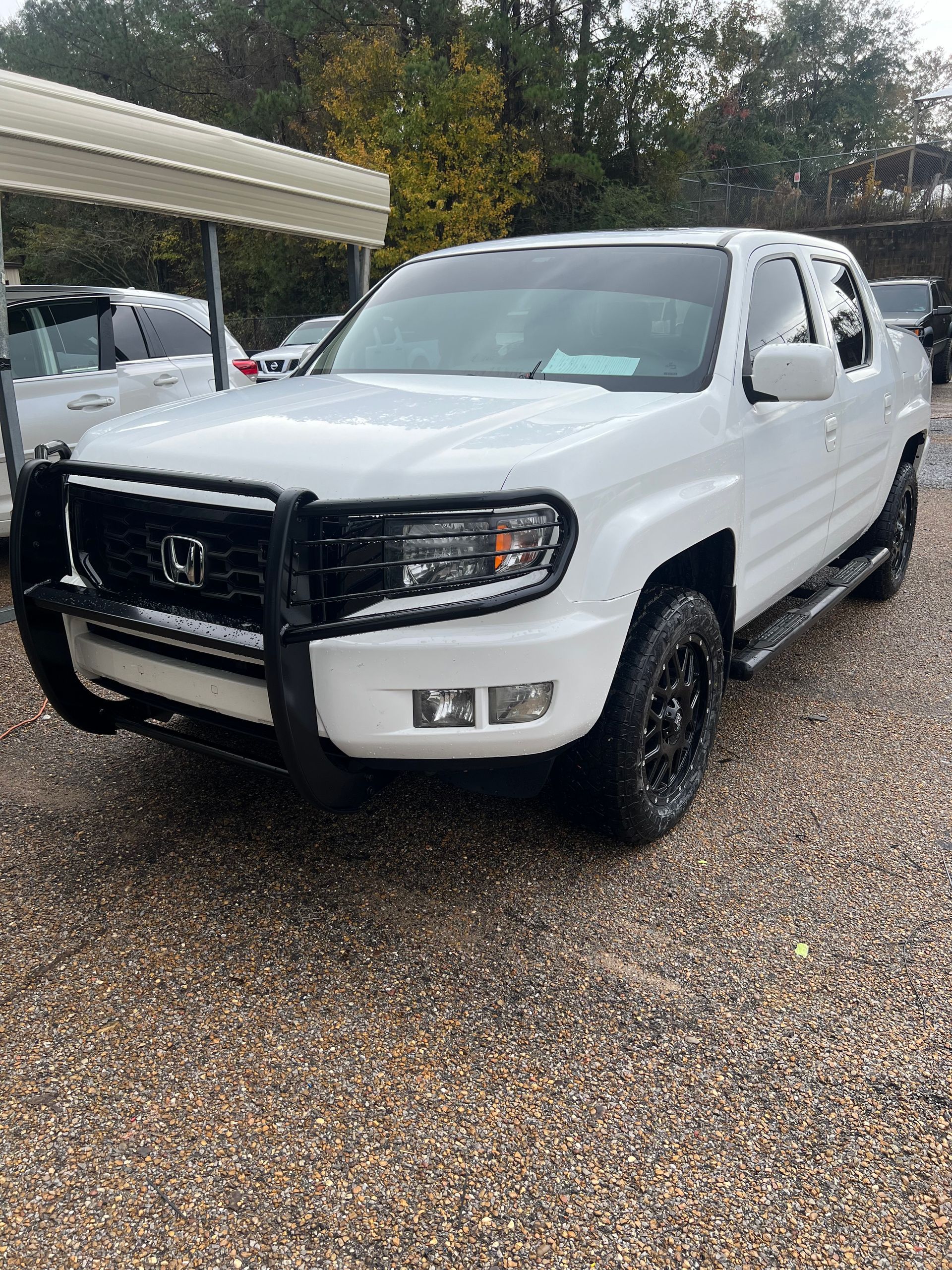 A white honda ridgeline pickup truck is parked in a gravel lot.
